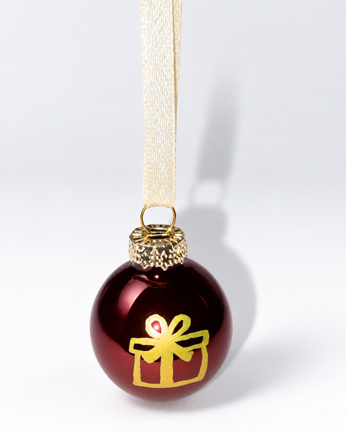 Handmade glossy dark brown glass Christmas ornament with gold gift box design and cream ribbon hanger