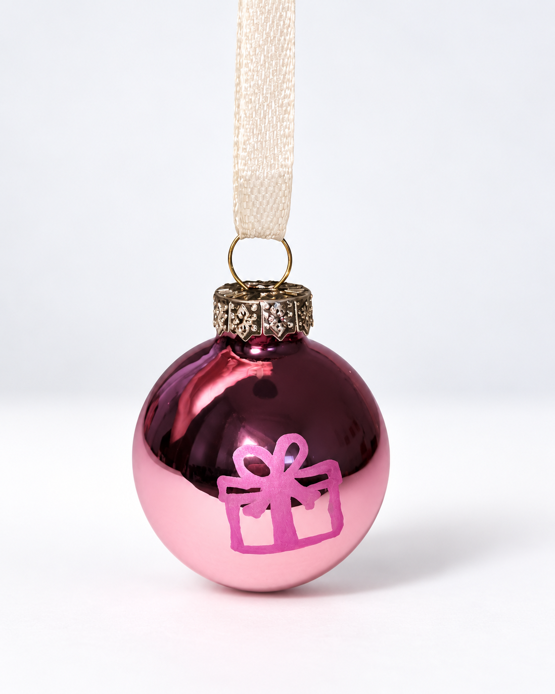 Handmade glossy pink glass Christmas ornament with pink gift box design and cream ribbon hanger