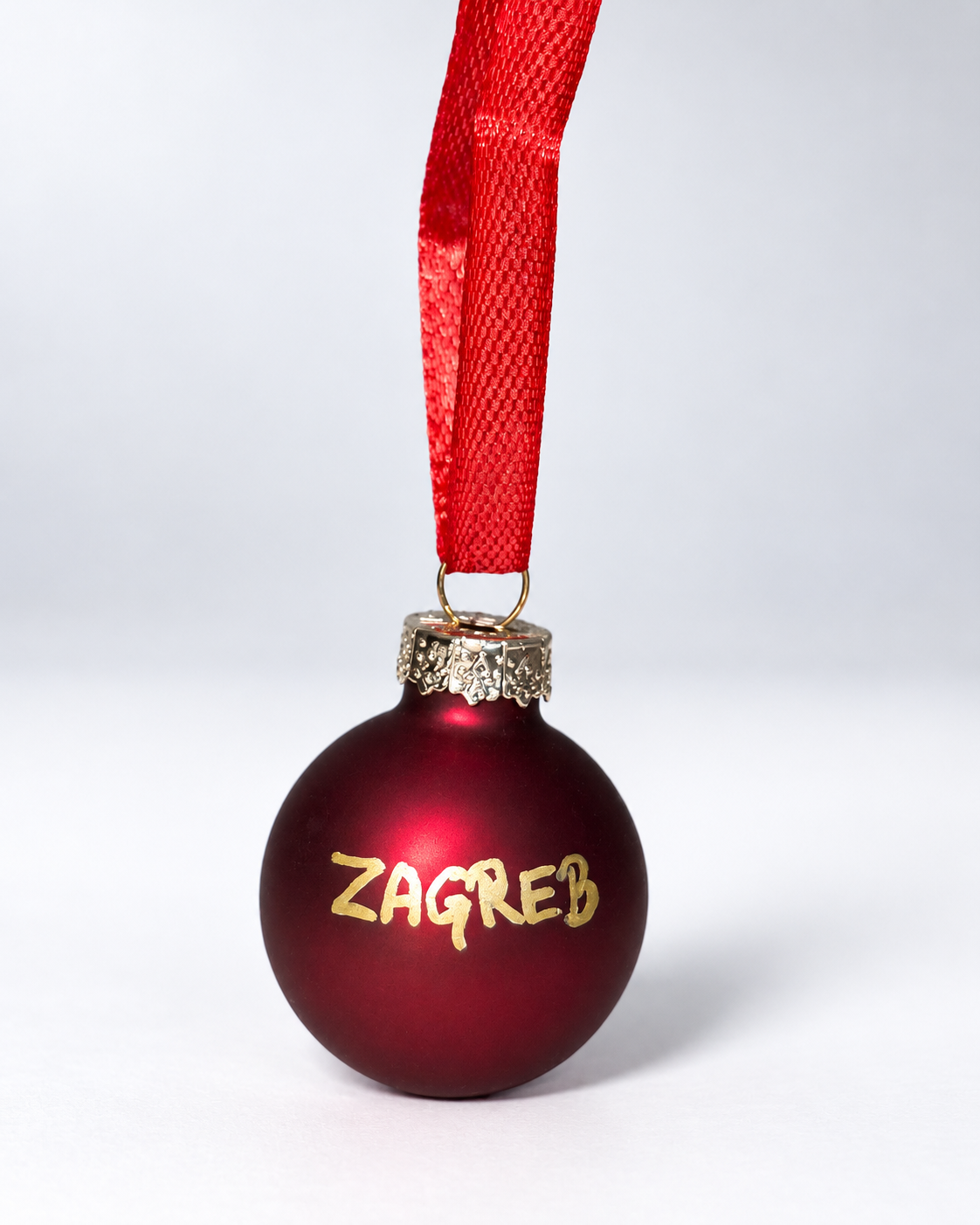 Handmade dark red glass Christmas ornament with gold ZAGREB lettering and red ribbon hanger